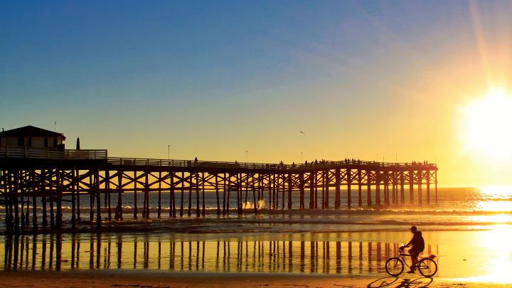 person riding their bike on the edge of the water underneath a pier.
