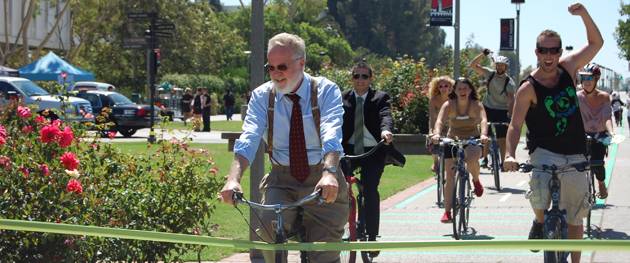 President Stephen L. Weber (far left) cuts the ribbon with his bicycle, opening the new campus bike/skate lane.
