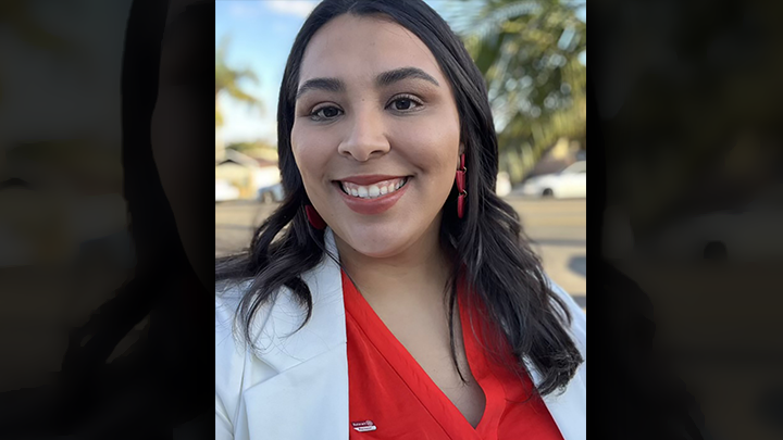 Stephanie Hernandez, dressed in a white jacket and red top, smiles for the camera during a photoshop.