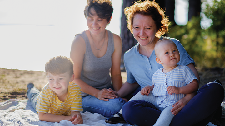 Two moms and their son and a daughter at an outdoor picnic near the sea during sunset.