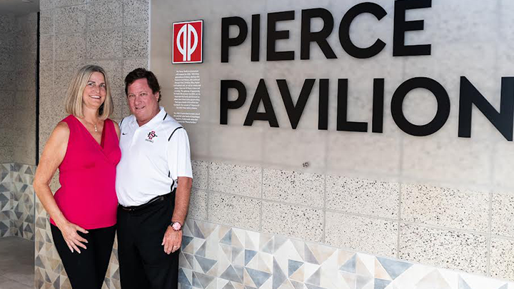 Christine and Fred Pierce smile for photo in front of the Pierce Pavilion sign at SDSU's Snapdragon Stadium.