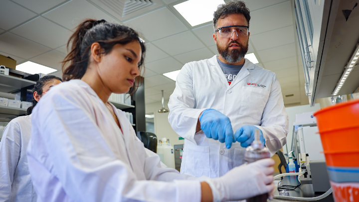 Maryam Fani and Matthew Verbyla dressed in white lab coats work inside a lab at SDSU analyzing soil samples for pollution indicators. (Rachel Crawford/SDSU)