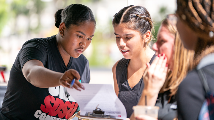 An SDSU student shows a registration form to a fellow student during an outdoor event on the campus.