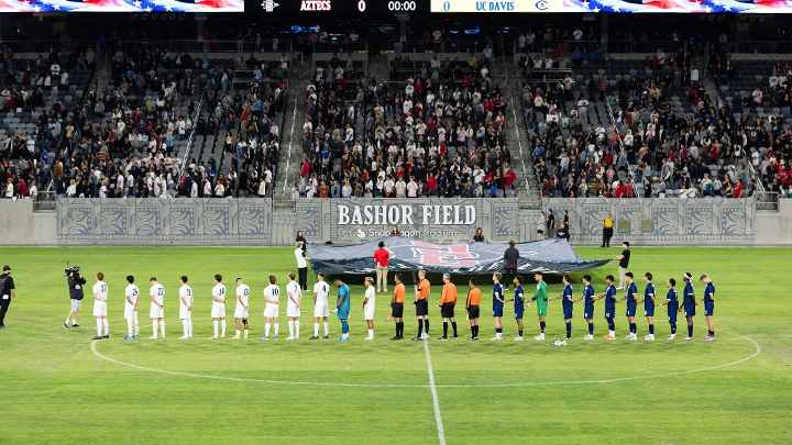 The SDSU and UC Davis men's soccer teams stand at midfield during the national anthem Saturday night at Snapdragon Stadium.