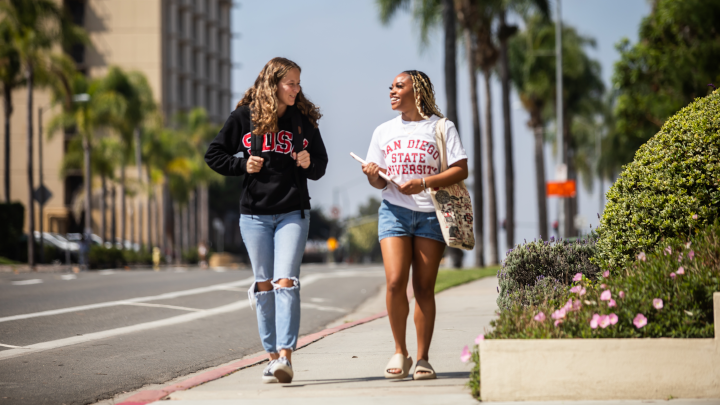 Two female students walk along a pathway outside the SDSU campus during a sunny day in San Diego.