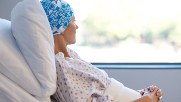 Photo shows patient dressed in a gown laying in their bed in a hospital room looking out the window.