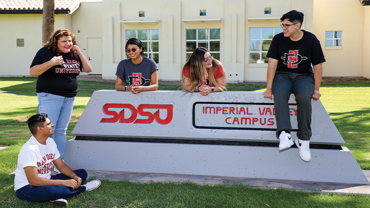 A group students surround the SDSU Imperial Valley sign outside of the campus' main entrance