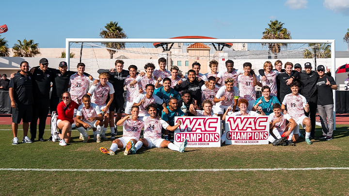 San Diego State’s soccer team dressed in their white uniforms and holding up a champions banner pose for a photograph in front of the goal after the game.