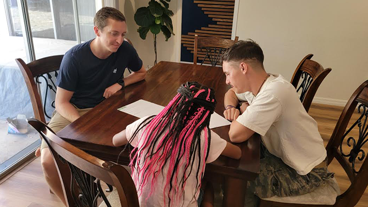 SDSU alumnus Michael Dalman sits a dining table at home with his foster daughter and tutor Isaac