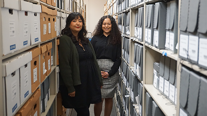 Erika Esquivel and Natalie Santizo standing in an aisle between large bookshelves.