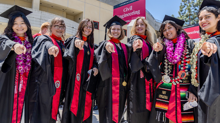 Graduates in their caps and gowns smile toward the camera.