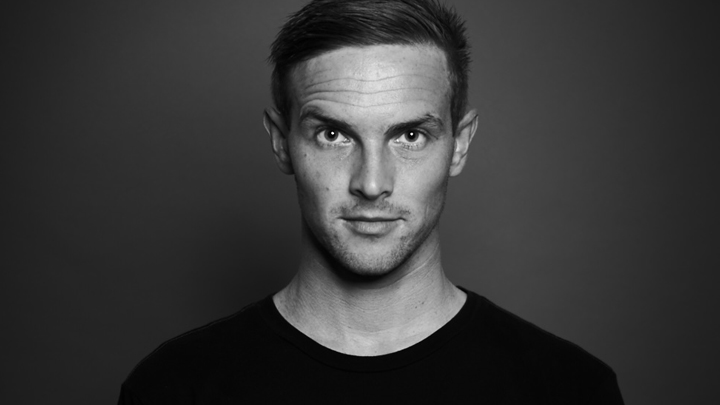 A black and white photograph of SDSU alumni Jeff Lewis smiling at the camera in a studio