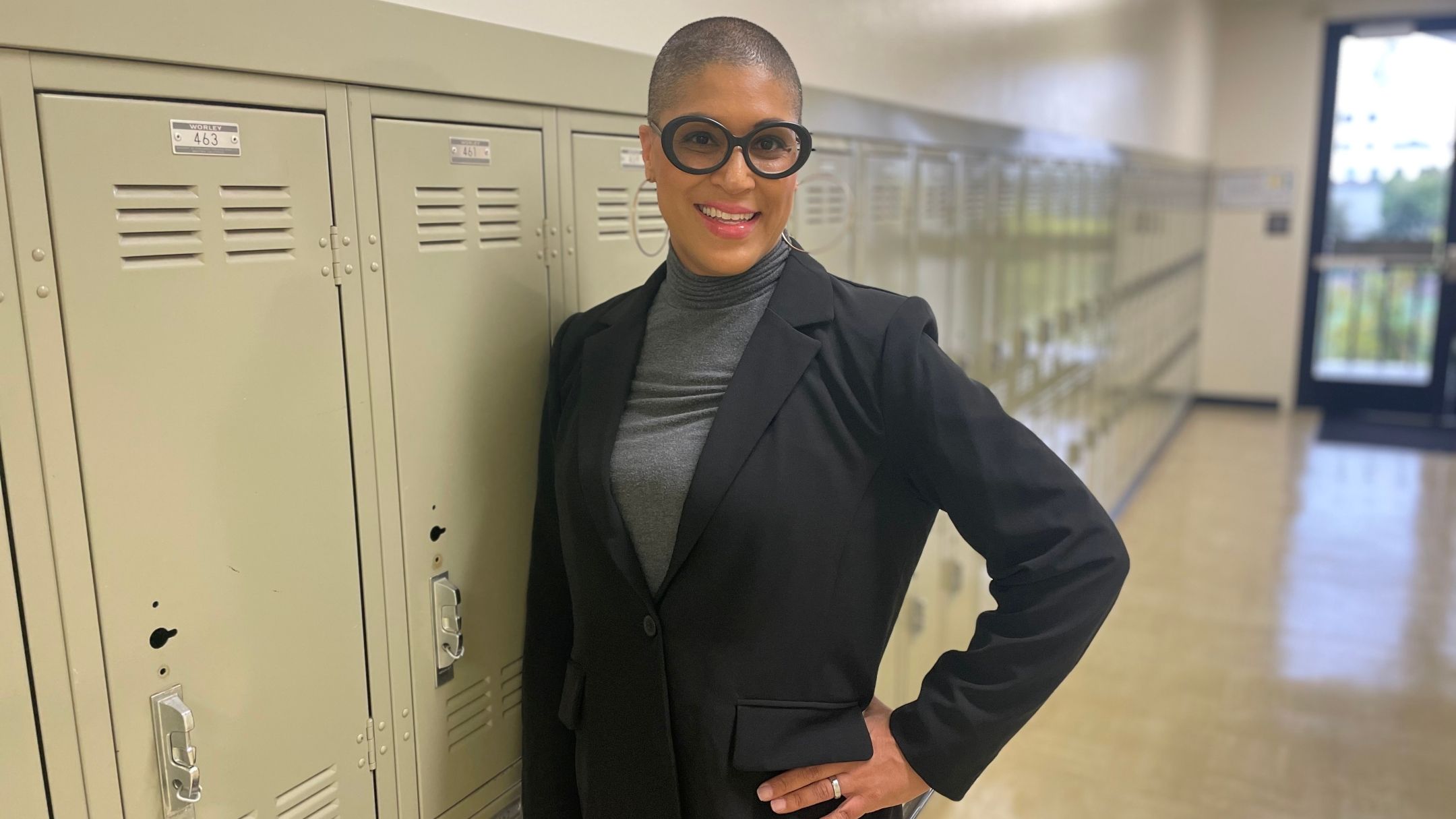 Acacia Thede photographed standing in front of a wall of lockers inside a school hallway.