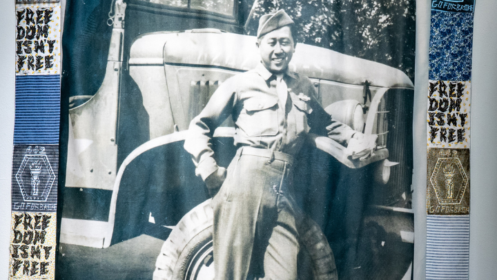 A black and white image of a Japanese soldier in uniform leaning against a military vehicle