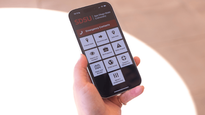 A closeup image of a left hand holding a smartphone with a screen depicting Emergency Contacts and ten boxes below.